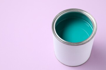 Can of turquoise paint on violet background, closeup. Space for text