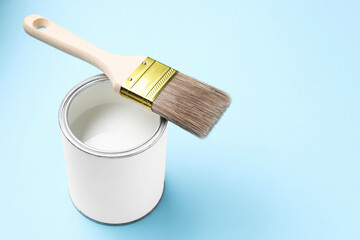 Can of white paint and brush on light blue background, closeup. Space for text