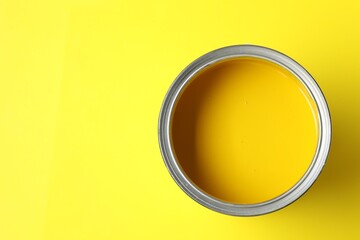 Can of bright paint on yellow background, top view. Space for text
