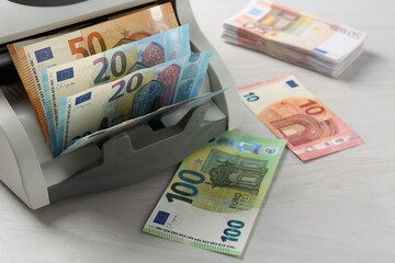 Money counter machine with euro banknotes on white wooden table, closeup