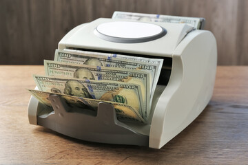 Money counter machine with dollar banknotes on wooden table, closeup