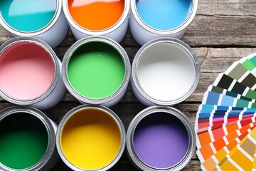 Cans of bright paints and color palettes on wooden table, flat lay