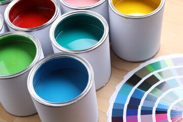 Cans of bright paints and color palettes on wooden table, closeup