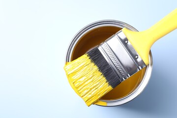 Can of yellow paint and brush on light background, top view. Space for text