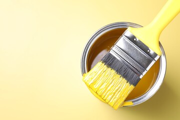 Can of paint and brush on yellow background, top view. Space for text