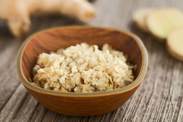 Freshly grated ginger in small bowl with ginger root and slices  in the back (Selective Focus,...