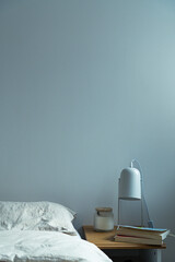 Minimalist bedroom interior with books, candle and lamp on nightstand