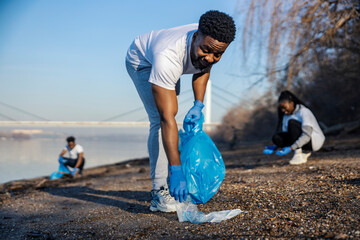 Young black eco aware activists cleaning riverbank from trash.