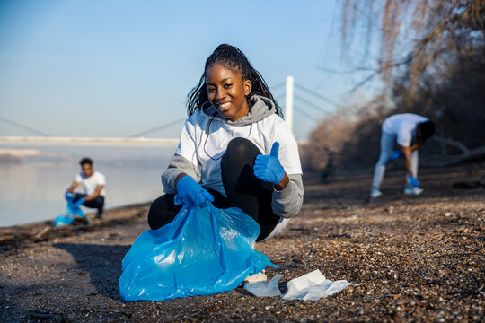 Portrait of multicultural eco volunteer cleaning riverside and giving thumbs up at the camera.