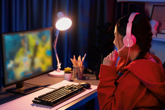 Host channel of young beautiful Asian gaming streamer playing fighting Moba at battle arena game on pc screen with multiplays, wearing pastel headphone at neon digital light modern room. Stratagem.