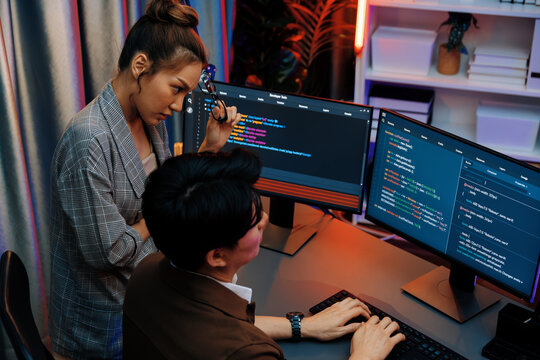 IT developers discussing with point to intelligent website development coder system running data online on pc of two screens with information technology at neon light room at modern office. Infobahn.