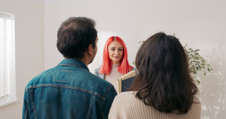 A young pair visits a real estate agent to view a modern renovated apartment. The woman with pink hair shows them around while they discuss renting or buying.