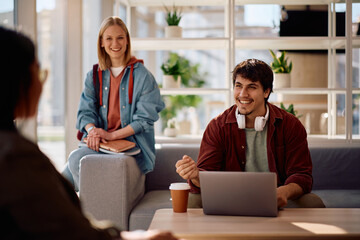 Happy college student using laptop while studying with his friends at campus.