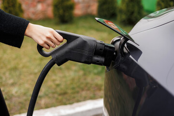 Unrecognisable woman inserting EV charger plug from public or home charging station for modern...