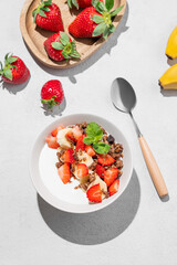 Natural Greek yogurt with homemade chocolate granola, strawberries and banana in a bowl on a light background
