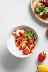 Natural Greek yogurt with homemade chocolate granola, strawberries and banana in a bowl