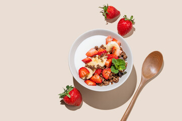 Greek yogurt with chocolate granola, strawberries and banana in a bowl on a beige background