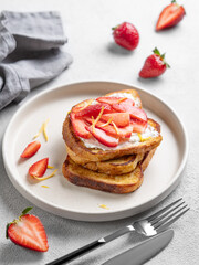 Toasted bread with cream cheese and strawberries on a plate on a light background with fresh berries.