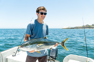 A young brunette with glasses smiles proudly while holding a large fish freshly caught from the...