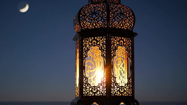 Intricate metal lantern with a burning candle inside, casting a soft glow on a wooden table under a night sky with a crescent moon. Perfect for religious and cultural themes.