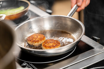 Golden-brown patties sizzling in oil inside a stainless steel pan on a stovetop, showcasing the cooking process of homemade food preparation.