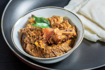 Rice Pathiri with beef masala or roast, a Kerala-style homemade recipe, garnished with curry leaves and served in a white bowl against a black background.
