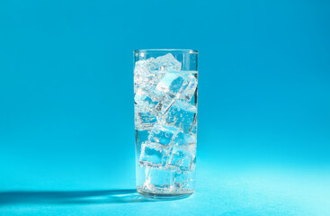 Soda water with ice cubes in glass on light blue background
