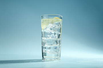 Soda water with lemon and ice cubes in glass on light blue background