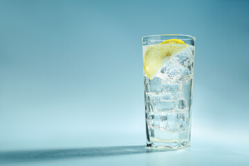 Soda water with lemon and ice cubes in glass on light blue background, space for text
