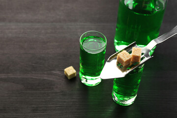 Absinthe in shot glasses, bottle, brown sugar and slotted spoon on wooden table, closeup. Space for...