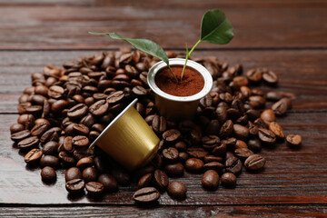 Coffee capsules with leaves and beans on wooden table, closeup