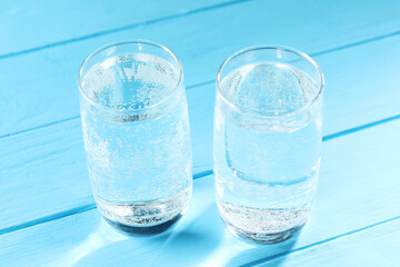 Refreshing soda water in glasses on light blue wooden table, closeup