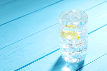 Refreshing soda water with ice cubes and slice of lemon in glass on light blue wooden table, closeup. Space for text