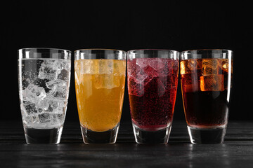 Refreshing soda water of different flavors with ice cubes in glasses on black wooden table
