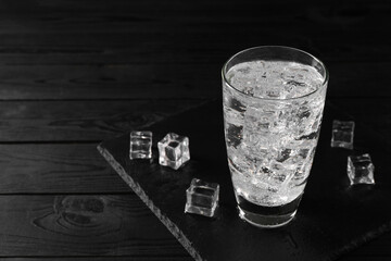 Refreshing soda water in glass with ice cubes on black wooden table, space for text
