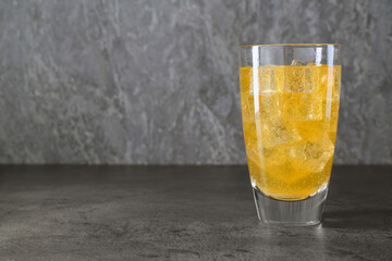 Sweet soda water with ice cubes in glass on grey table, space for text