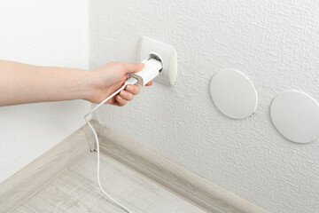Woman plugging USB power adapter with charge cable into electrical socket indoors, closeup