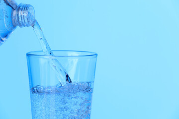 Pouring soda water from bottle into glass on light blue background, closeup. Space for text