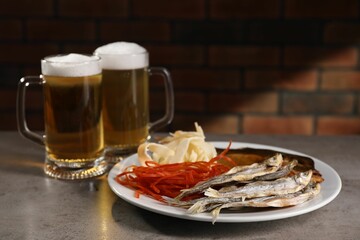 Different dried fish snacks and beer on grey table. Space for text