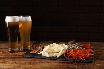 Different dried fish snacks and beer on wooden table. Space for text