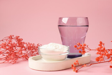 Collagen powder in bowl, glass of water and gypsophila branches on pink background, closeup