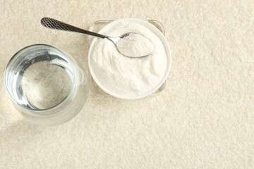 Collagen powder in bowl, spoon and glass of water on light textured table, flat lay. Space for text