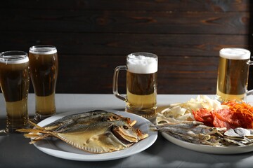 Dried fish and glasses of beer on grey textured table against wooden background, closeup