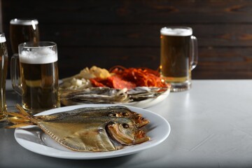 Dried fish and glasses of beer on grey textured table against wooden background, closeup