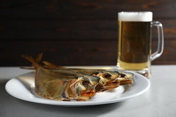 Dried fish and glass of beer on grey textured table against wooden background, closeup