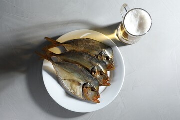 Dried fish and glass of beer on grey textured table, flat lay