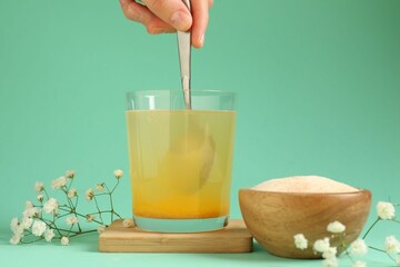 Woman stirring collagen powder in water on turquoise background, closeup
