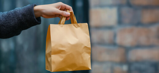 Close-up of female hand holding brown paper bag against brick wall background