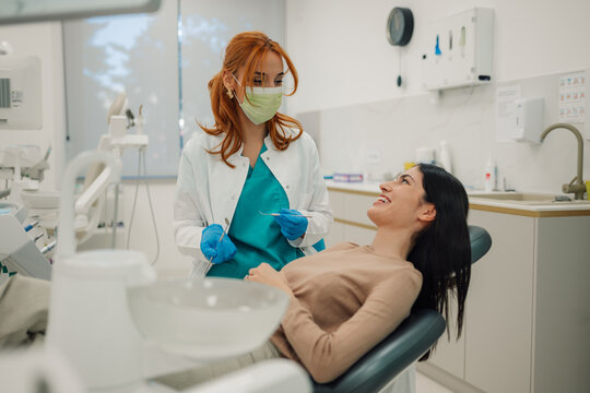 Female dentist wearing surgical mask holding dental tools talking to patient