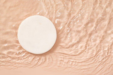 Decorative round marble white podium for cosmetics in water with splashes and waves in sunlight on...